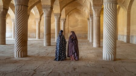 Shiraz, Iran - May 2019: Two Iranian women talking in prayer hall of Vakil Mosque with columns. Vakil means regent, title of Karim Khan, founder of Zand Dynasty.のeditorial素材