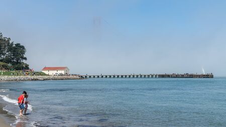 San Francisco, USA - August 2019: Golden Gate Bridge inside fog, barely visible, with children playing on the beachのeditorial素材