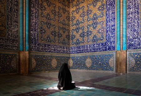 Isfahan, Iran - May 2019: Unidentified Iranian woman wearing chador praying inside Sheikh Lotfollah Mosque with tiles on walls, Isfahan, Iranのeditorial素材