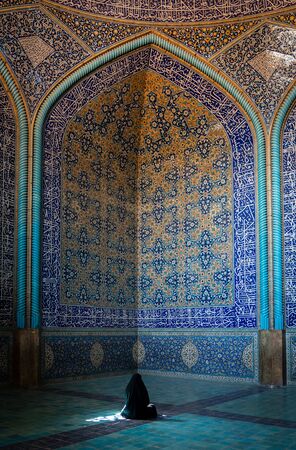 Isfahan, Iran - May 2019: Unidentified Iranian woman wearing chador praying inside Sheikh Lotfollah Mosque with tiles on walls, Isfahan, Iranのeditorial素材