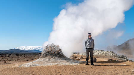 Hverir, Iceland - May 2019: Tourist standing next to a steam vent in Hverir Myvatn geothermal area, exploring natural steam vents and mud pools all around Lake Myvatn, the Hverir geothermal fieldのeditorial素材