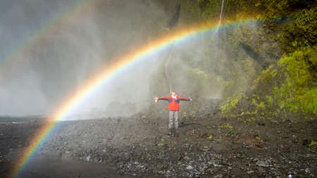 Skogar, Iceland - May 2019: Man standing under the rainbow at Skogafoss waterfall areaのeditorial素材