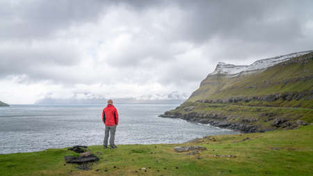 Unidentified man looking at the dramatic landscape in Faroe Islands, Denmarkのeditorial素材