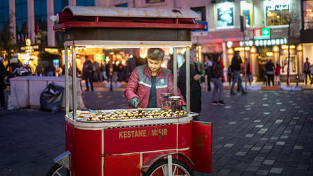 Istanbul, Turkey - November 2019: Man selling roasted chestnut in Taksim district with crowded people walking in Istiklal street, Istanbul city lifeのeditorial素材