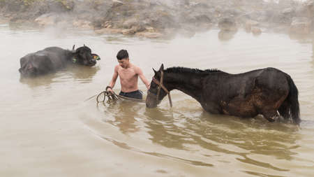 Guroymak, Bitlis, Turkey - February 2020: Young boy and his horse in thermal water, friendship with domestic animals, animal showerのeditorial素材