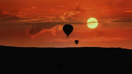 Silhouettes of hot air balloons flying in Cappadocia landscape with dramatic morning sky, Turkeyの写真素材