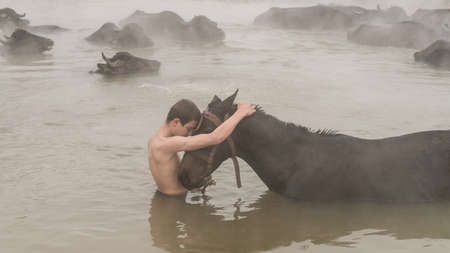 Guroymak, Bitlis, Turkey - February 2020: Young boy and his horse in thermal water, friendship with domestic animals, animal showerのeditorial素材