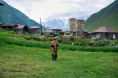 Ushguli, Georgia - August 2015: Georgian old woman walking in Ushguli village with rock tower houses in Svaneti, Georgia. These are typical Svaneti defensive tower houses found throughout the villageのeditorial素材
