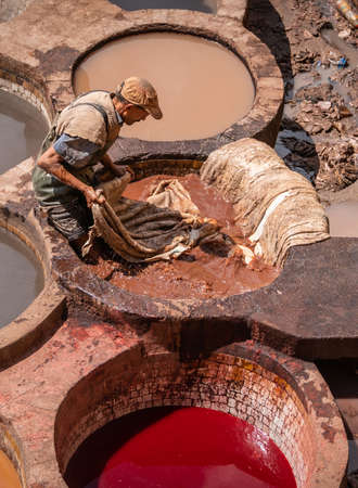 Fez, Morocco - April 2018: Tanner working in the dye pots at Chouara Tannery painting animal leathers. Round stone wells filled with dye or white liquids for softening the hides.のeditorial素材