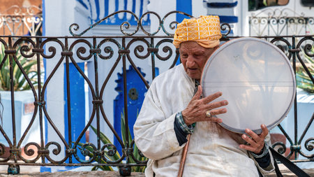 Chefchaouen, Morocco - 11 September 2022: Old man playing a traditional instrument in Chefchaouen, known as the blue city, famous for its striking blue color painted medina buildings and streetsのeditorial素材
