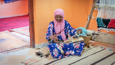 Fes, Morocco - 14 September 2022: Senior woman spining a woolen string for a Moroccan carpet. A Moroccan carpet is a handwoven masterpiece, crafted by skilled artisans.のeditorial素材