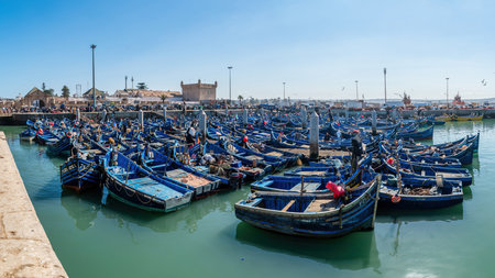 Essaouira, Morocco - 17 September 2022: Traditional blue fishing boats docked in port of Essaouira. Fishing boats line the harbor, bringing in the day's catch, while seagulls circle overheadのeditorial素材