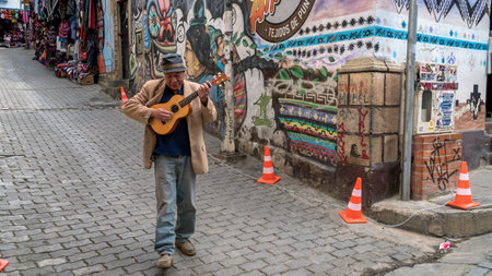 Cusco, Peru - 24 October 2023: A Peruvian man playing a guitar and singing, walking in city streetのeditorial素材