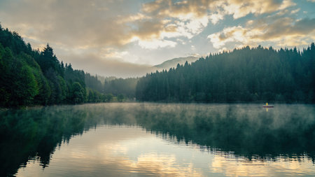 Artvin, Turkey - 8 October 2021: Man in a boat in Savsat Karagol Black lake in Black Sea region with morning evaporation. Savsat Karagol lake is a large trout lake in the forest in Artvinの写真素材