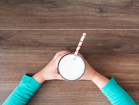 Child holding a glass of milk on wooden backgroundの写真素材
