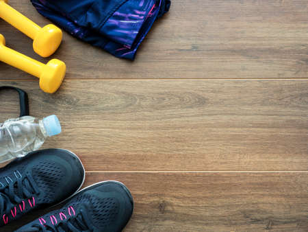 Healthy lifestyle concept background with running shoes, water, dumbbells, smart band and clothes on wooden backgroundの写真素材