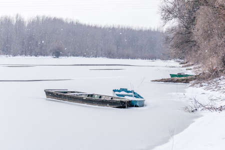 Moored wooden fishing boat on the bank of the Danube tributary in frozen water.の写真素材