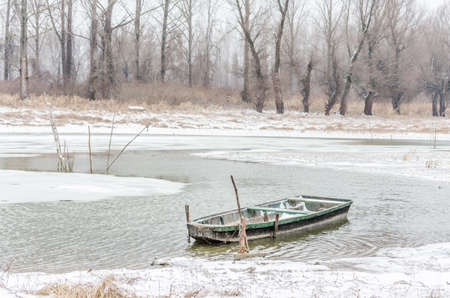 Moored wooden fishing boat on the bank of the Danube tributary in frozen water.の写真素材