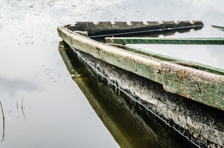 Wooden fishing boats tied to the shore. A view of a small wooden derelict fishing boat, moored at the shore of the lake in autumn.の写真素材
