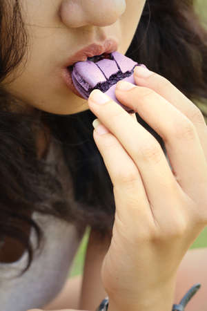 Woman eating a macaron at the park.の写真素材
