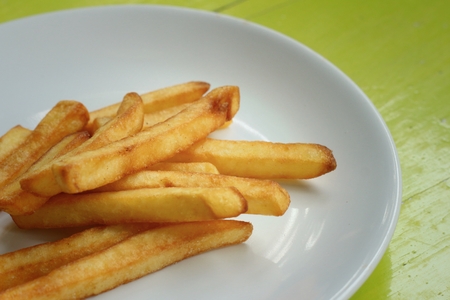 French fries in white plate on green background.