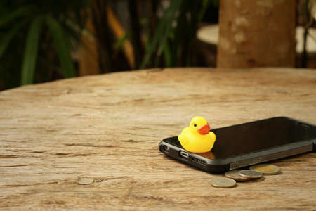 Smart phone with yellow rubber duck on background of wooden.の写真素材