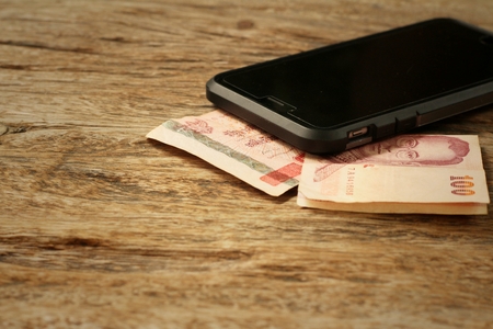 Smart phone with money of Thai Bath on wooden background.の写真素材