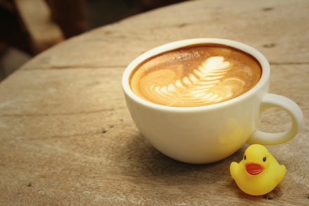 latte coffee with yellow rubber duck on background of wooden.の写真素材