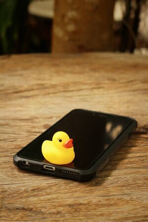 Smart phone with yellow rubber duck on background of wooden.