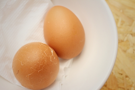 Broken eggs in white bowl on wooden background.
