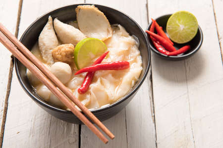Bowl of spicy soup with noodles and vegetables for a delicious appetizer served with chopsticks and surrounded by fresh ingredients.の写真素材