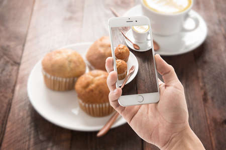 Taking photo of muffin and coffee on wooden table.の写真素材