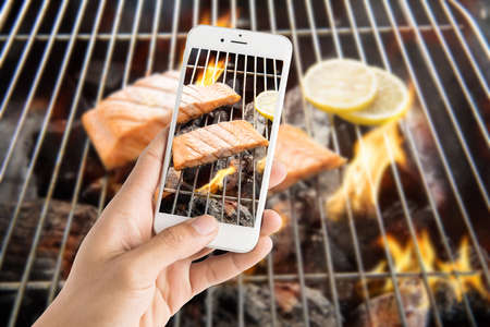 Taking photo of grilled salmon with lemon on the flaming grillの写真素材