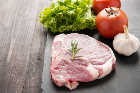 Raw pork on blackboard and vegetables on wooden background.の写真素材