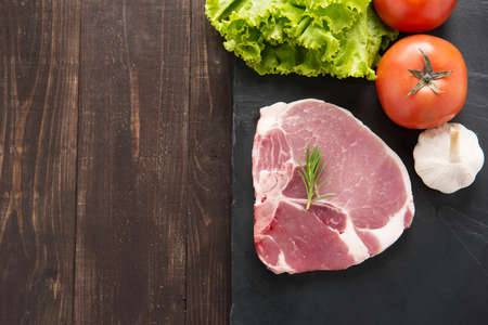 Top view raw pork on blackboard and vegetables on wooden background.