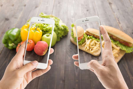 Friends using smartphones to take photos with contrasting foodの写真素材