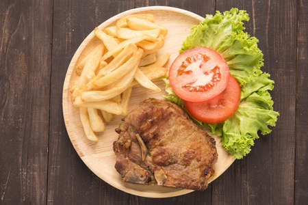 grilled pork chop steak and vegetables with french fries on wooden backgroundの写真素材