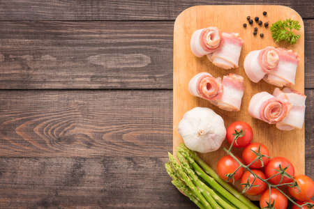 Bacon rolls with tomato, garlic, asparagus on wooden background.の写真素材