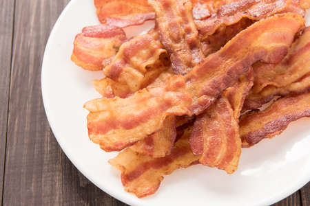 Closeup of fried bacon strips on white plate.の写真素材