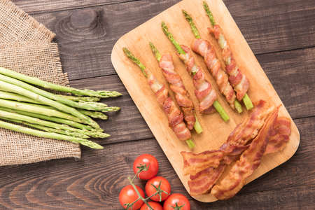 Asparagus wrapped in bacon with tomato on wooden background.の写真素材