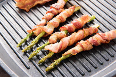 Bacon slice and asparagus wrapped in bacon being cooked in frying pan.の写真素材