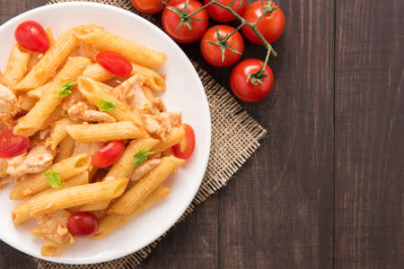 Penne pasta in tomato sauce with chicken on a wooden background.の写真素材