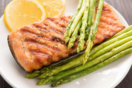 Grilled salmon with lemon, asparagus on the wooden background.の写真素材