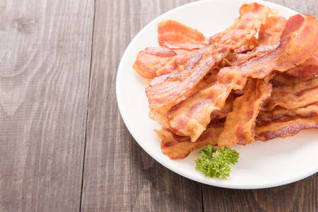 Closeup of fried bacon strips on white plate.