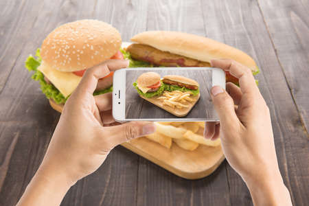 Friends using smartphones to take photos of hot dog and hamburger.