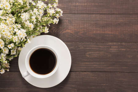 A cup of coffee with flowers on wooden background.