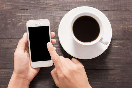 Using smartphone beside of coffee on wooden table.