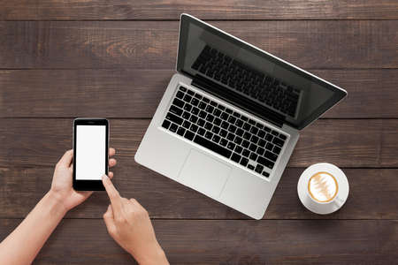 Using smartphone, tablet and a cup of coffee on wooden background.の写真素材