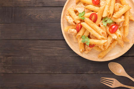 Penne pasta in tomato sauce with chicken on a wooden background. Copy space for text.の写真素材