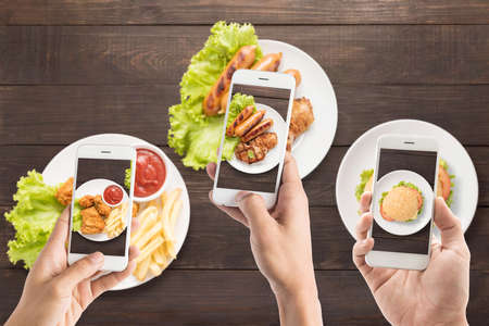 Friends using smartphones to take photos of sausage, pork chop, Fries chicken and burger.の写真素材